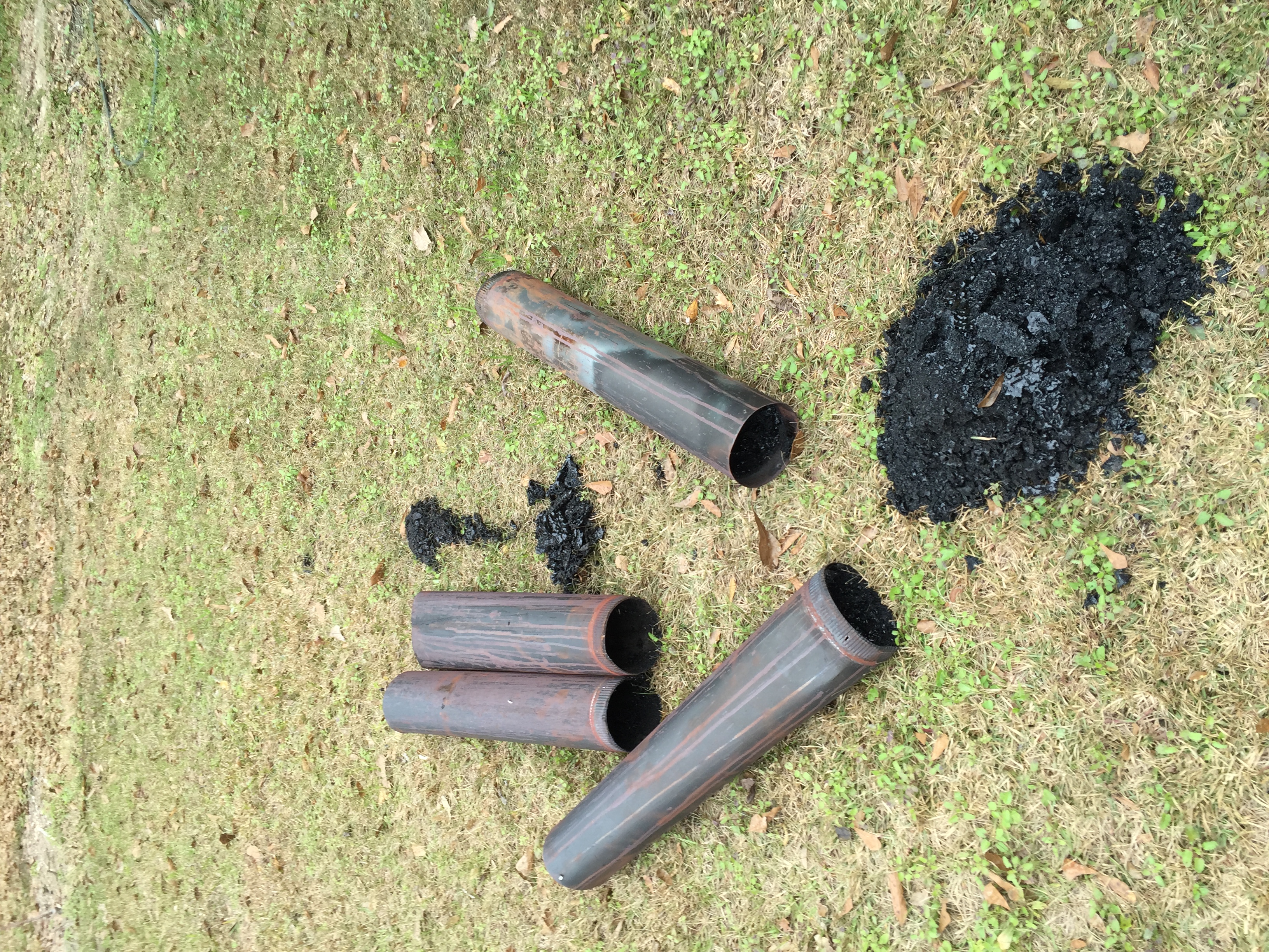 Chimney pipe after cleaning with heavy creosote buildup removed and piled beside the pipe.