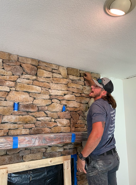 Skilled technician completing a stacked stone fireplace makeover with the final stone placement.