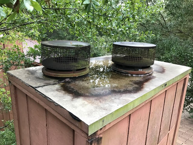 Rusted, flat chimney chase cover holding water and showing signs of corrosion before replacement.